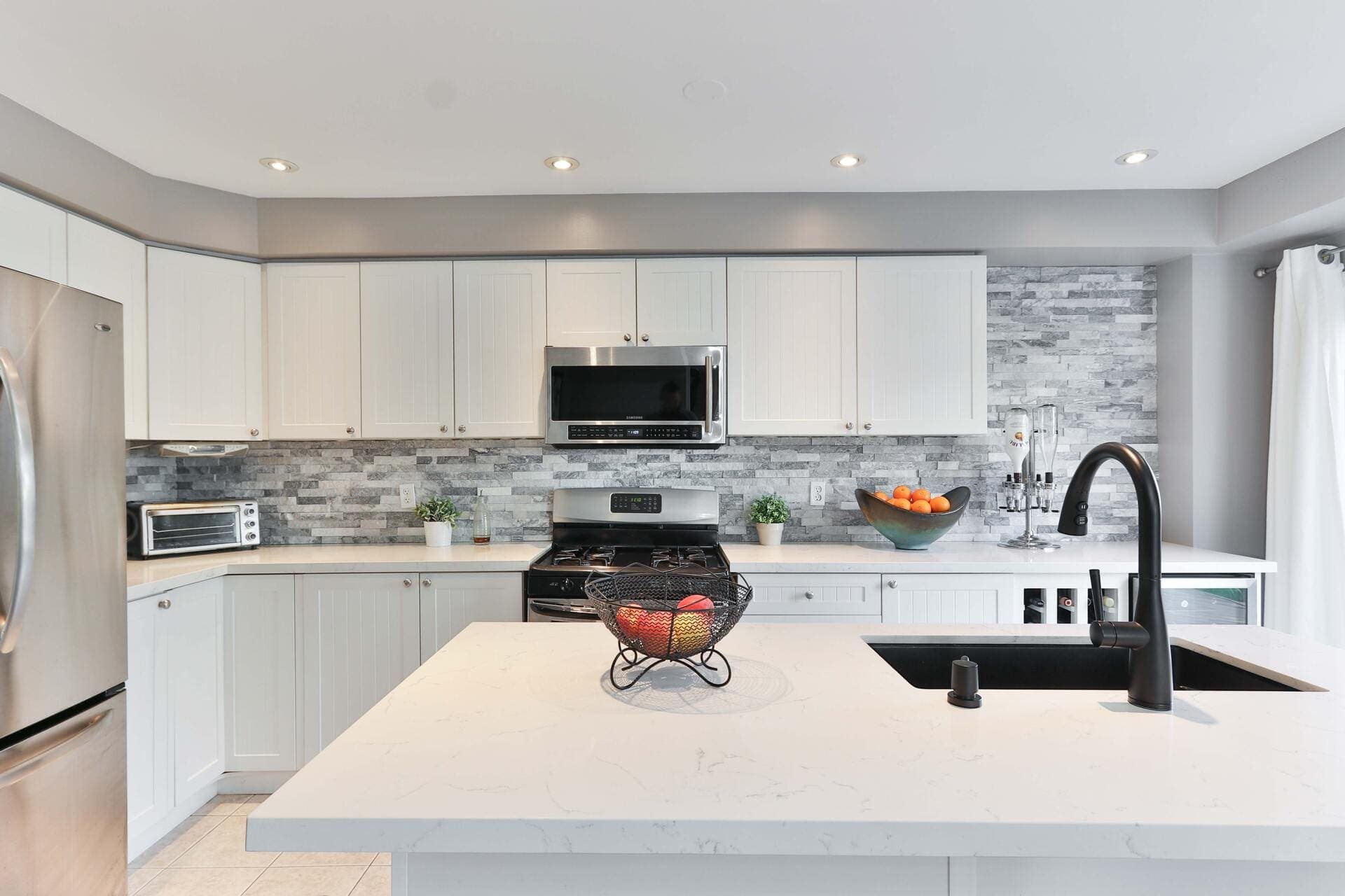 White kitchen with a stacked-stone tile backsplash behind the range