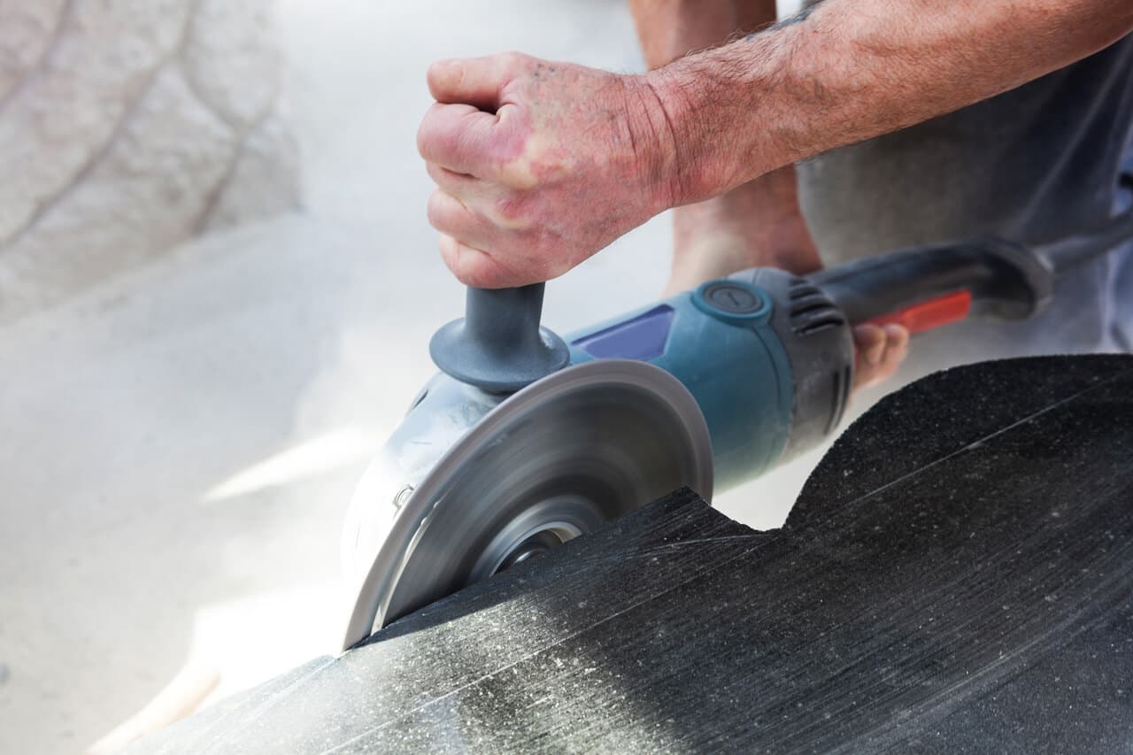 Hands guiding an angle grinder across a dark stone slab